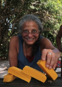 Ane Walsh smiling outdoors, arranging bright yellow blocks of natural material on a wooden table.